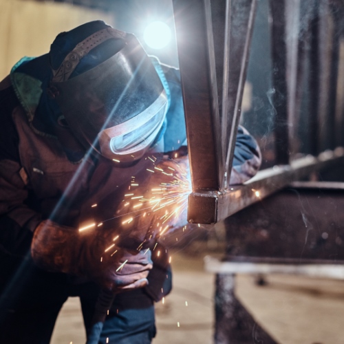 Man is working at metal factory, he is welding a piece of rail using special tools.